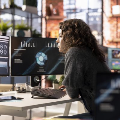 Young woman watching business conference infographics on computer screen, looking over statistics on online portfolio. Analyst in apartment looking at business presentation dashboard.