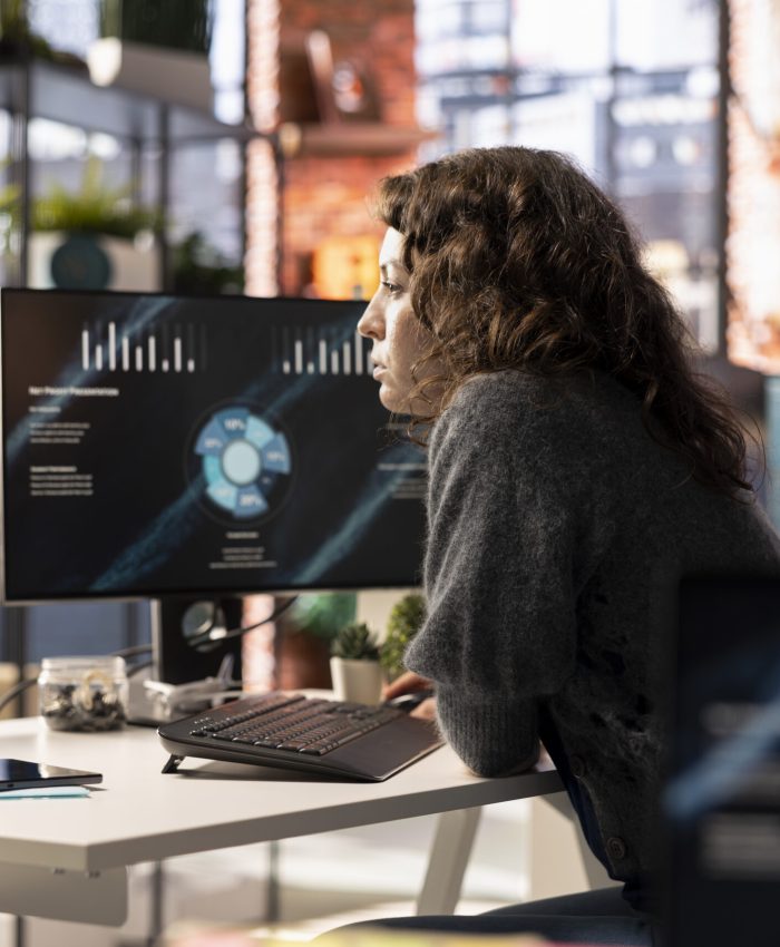 Young woman watching business conference infographics on computer screen, looking over statistics on online portfolio. Analyst in apartment looking at business presentation dashboard.